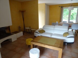 A living room with a white sofa, a wooden coffee table, a yellow ottoman, and a TV stand.