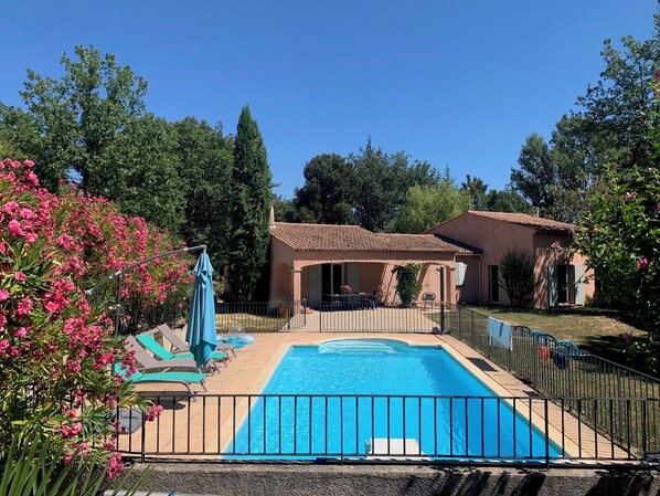 A swimming pool with a fenced deck, surrounded by a garden with pink flowers and trees. - Charming Provencal House - Private Pool - Near Lake & Beaches (Montauroux)