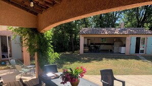 An outdoor patio with a table, chairs, and a laptop. There is a covered area with a kitchen visible in the background. - Charming Provencal House - Private Pool - Near Lake & Beaches (Montauroux)
