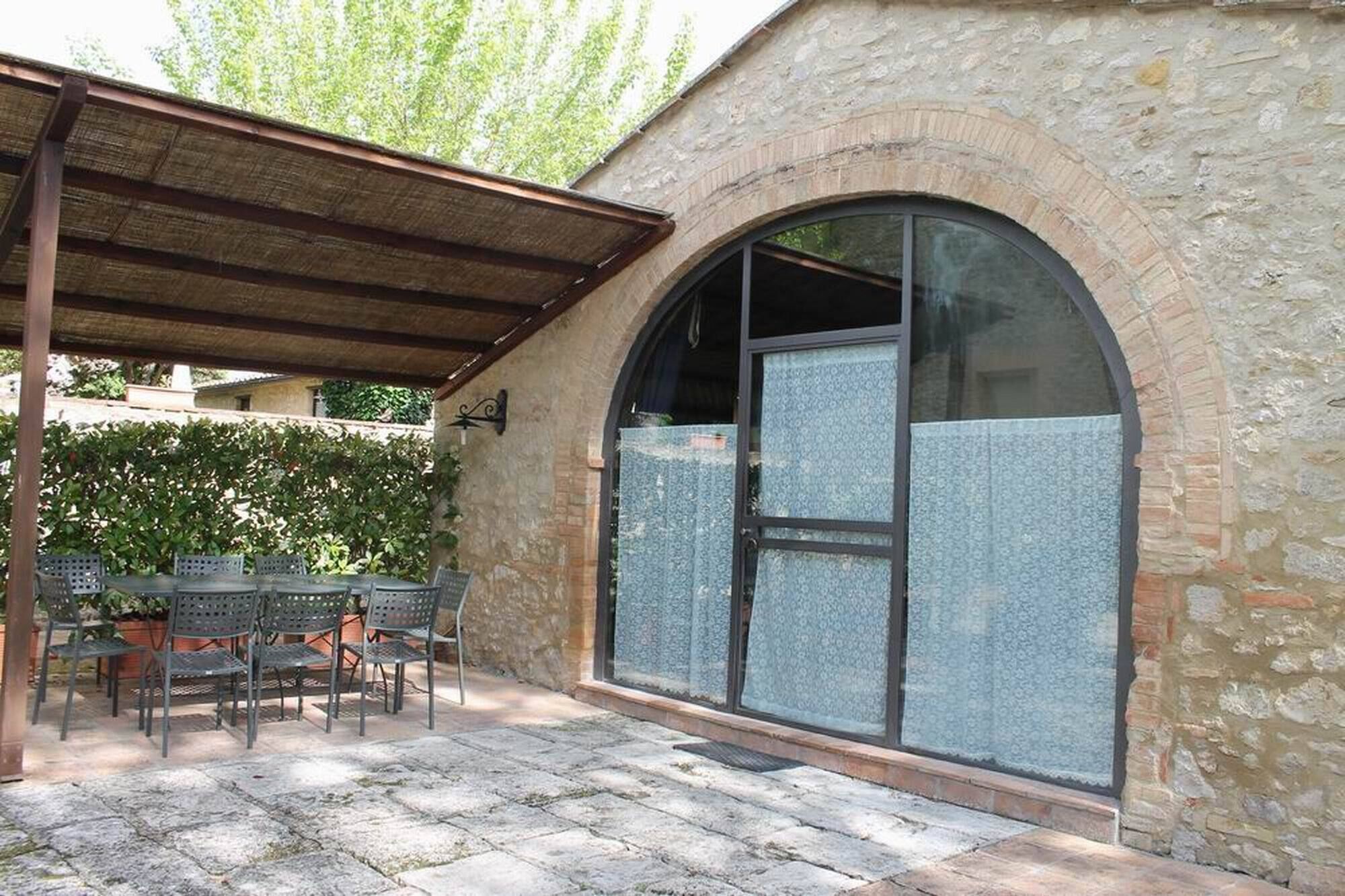 Un patio cubierto con suelo de piedra, una zona de estar con sillas de metal y un gran ventanal arqueado con paneles de vidrio esmerilado.