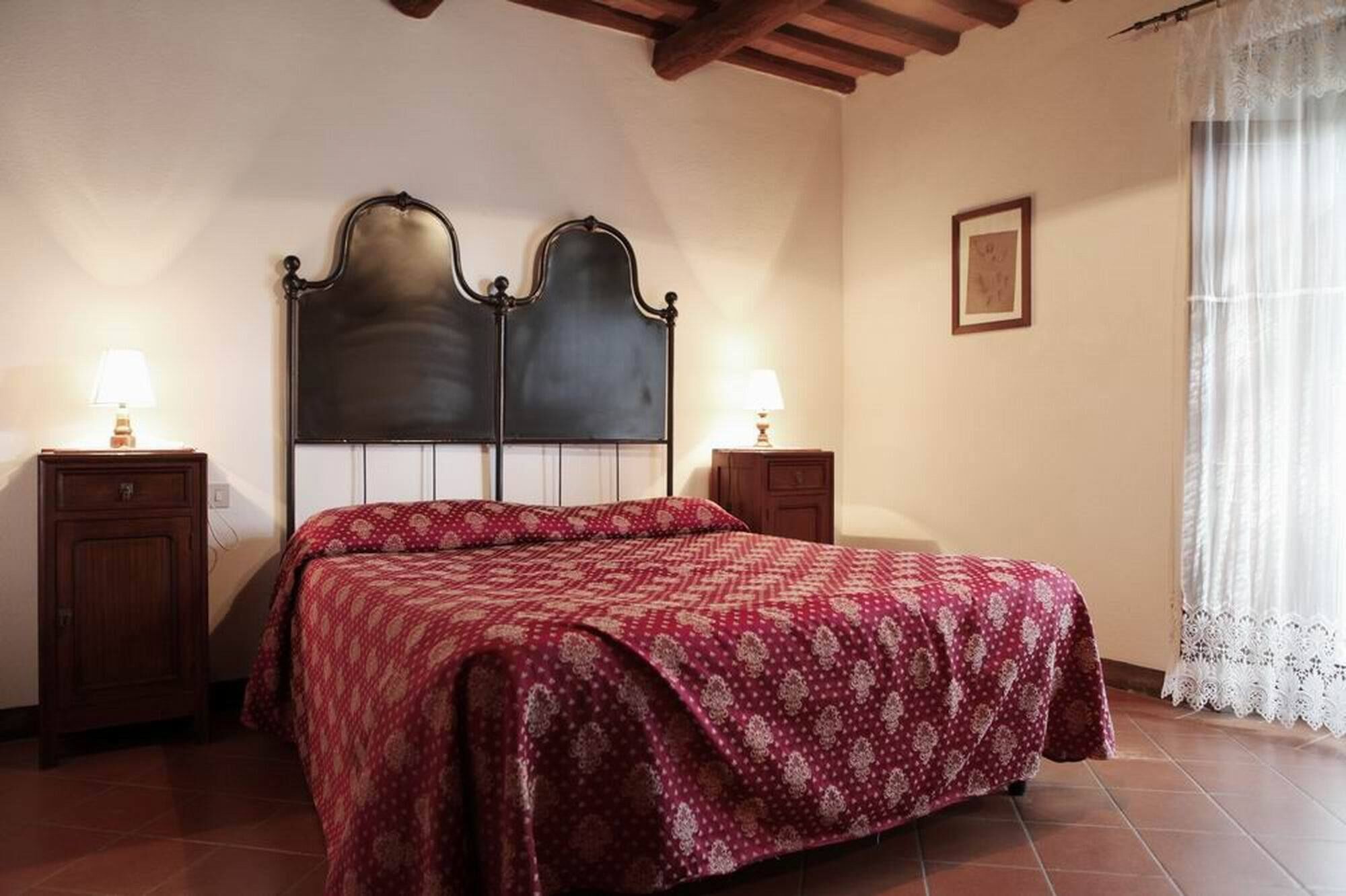 Quarto com uma cama grande, duas mesas de cabeceira, um painel de cabeceira de madeira, um quadro na parede e uma janela com cortinas leves.