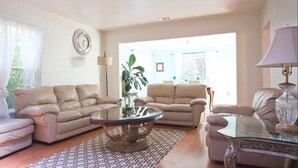 A living room with two sofas, a coffee table, and a lamp. There is a clock on the wall and a plant in the corner. - Easy Bay Hidden Gem (Richmond)