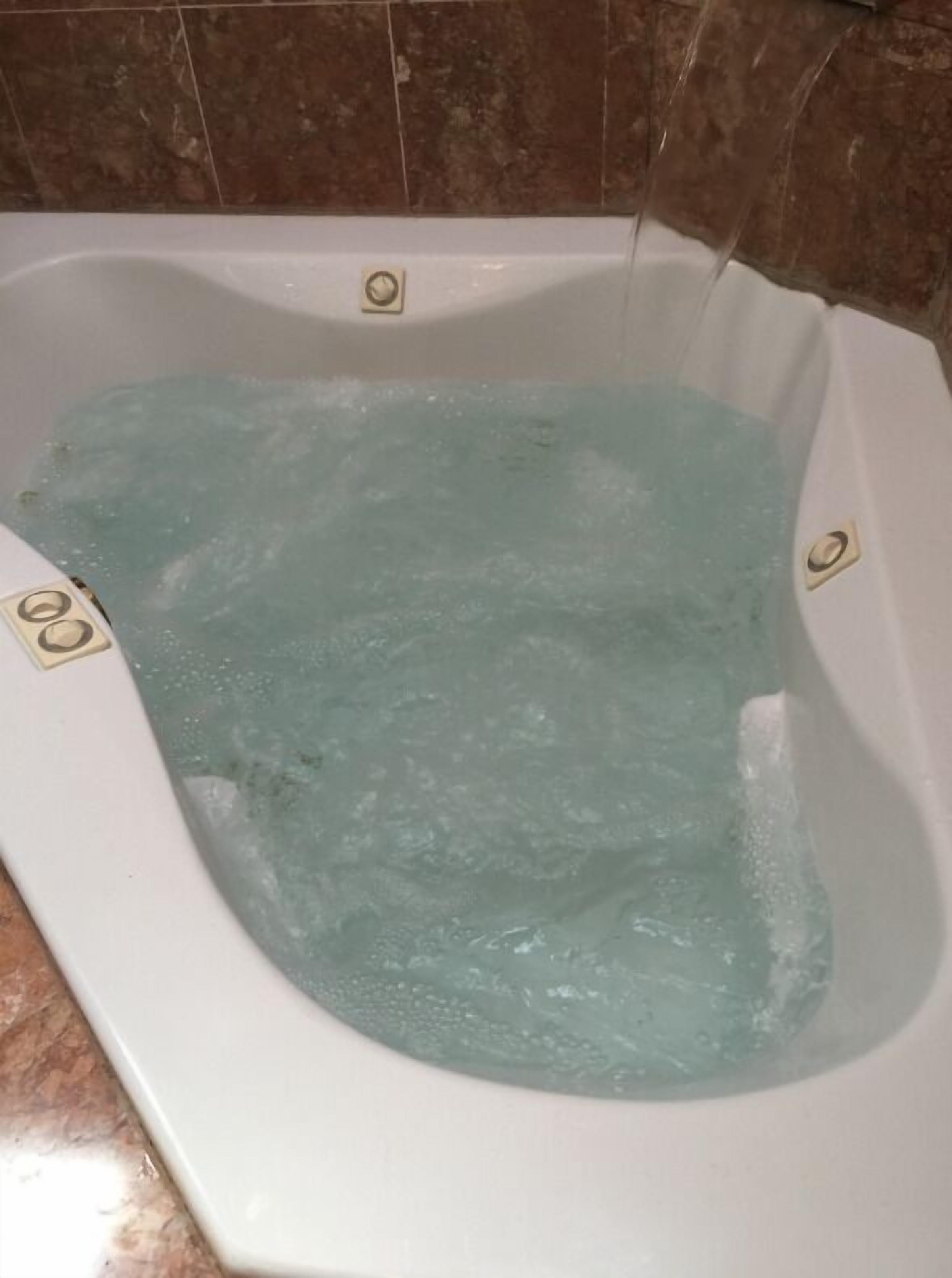 A hot tub with water running, set against a tiled wall.