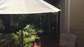A patio area with a beige umbrella, a potted plant, a chair, and a wooden deck.