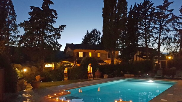 Una piscina con velas alrededor, una casa al fondo y árboles altos.