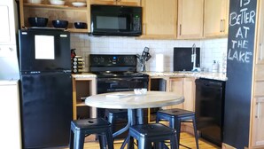 Una cocina con armarios de madera, un refrigerador negro, un microondas, una estufa y una pizarra con la frase 'Life is better at the lake'.