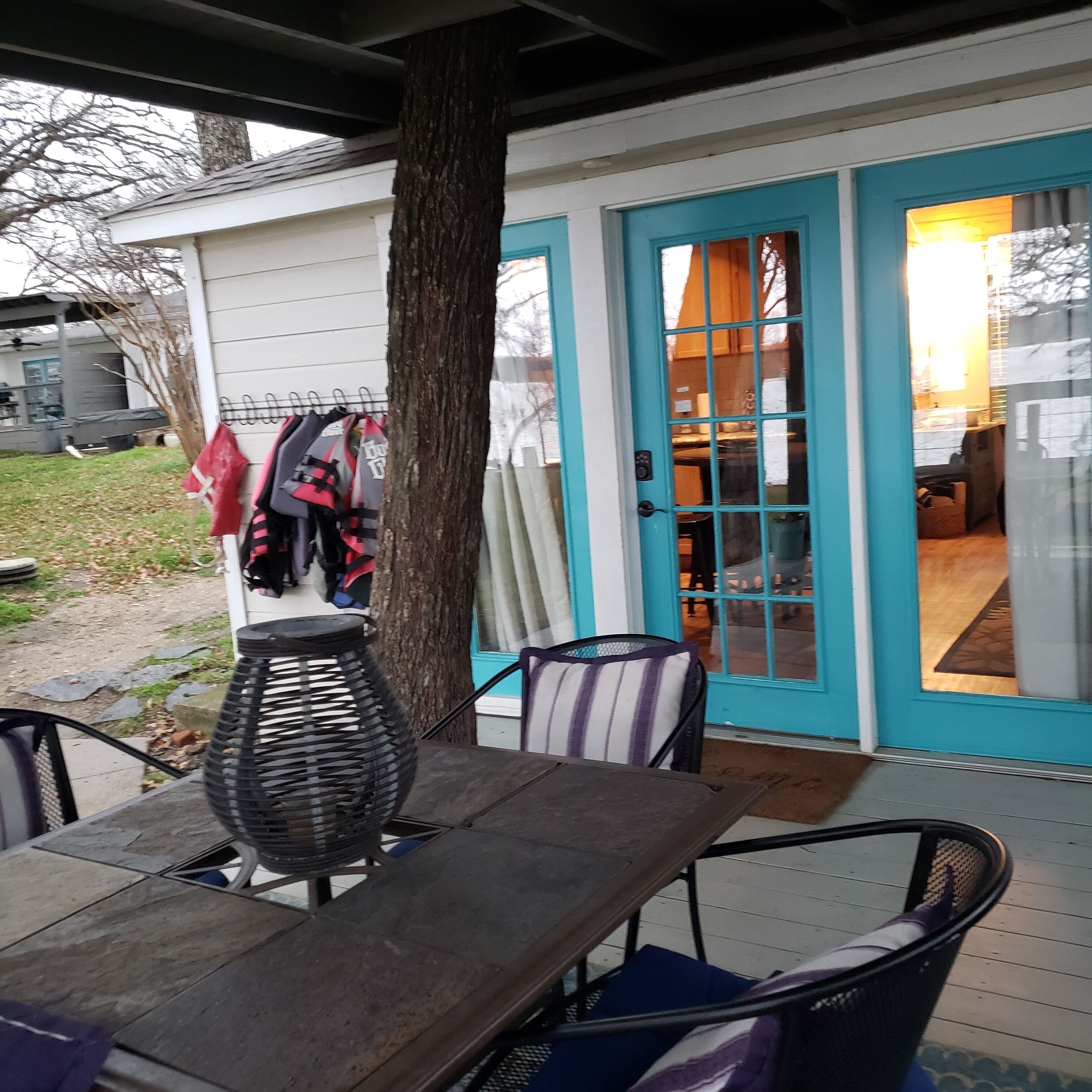 Un patio techado con una mesa, sillas y una silla de mimbre, y una puerta que da a un espacio interior.