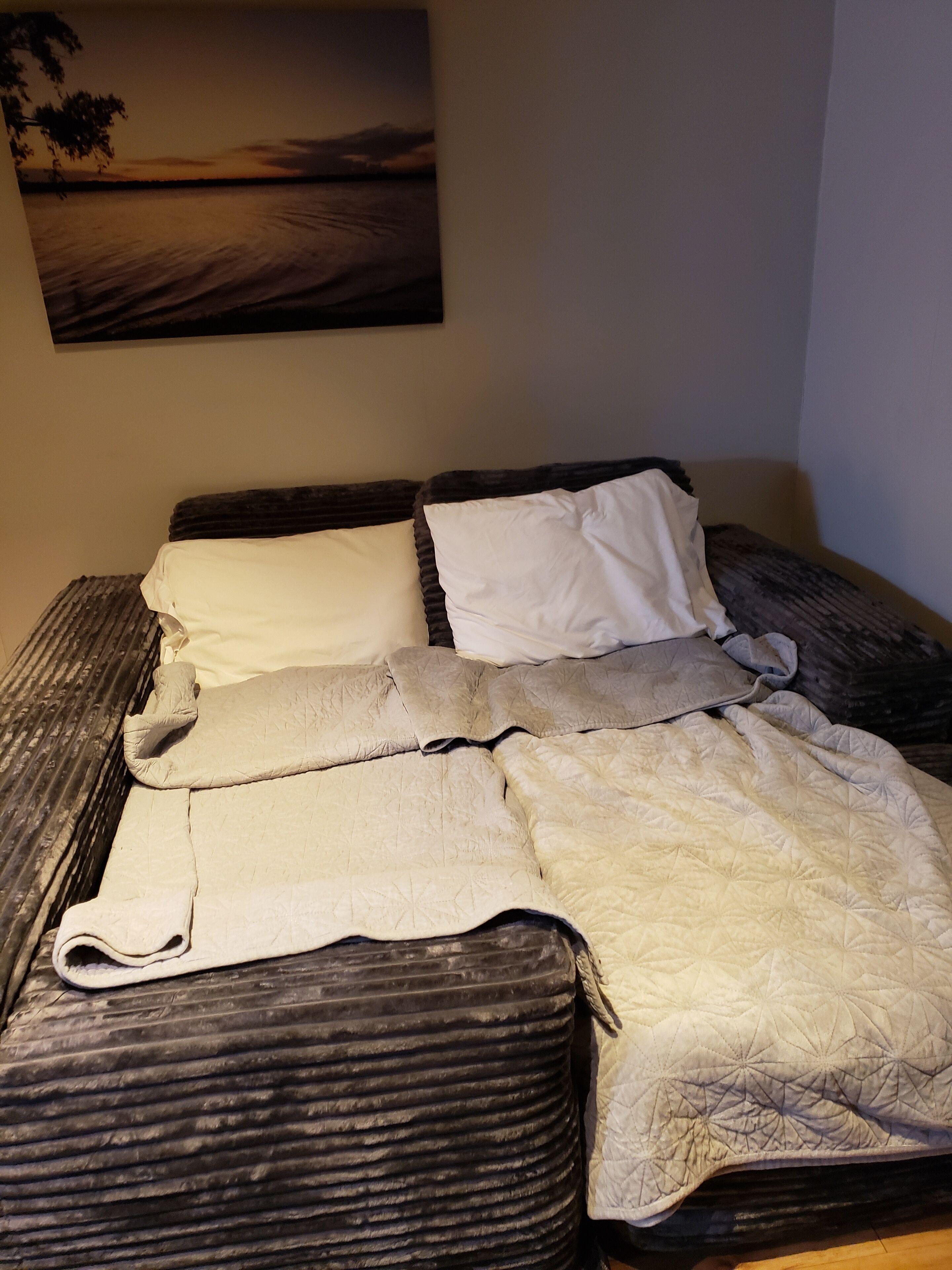A bed with a dark headboard, white pillows, and a beige quilt.