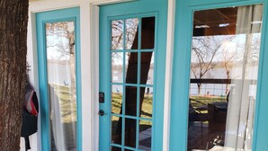Una puerta turquesa con un panel de vidrio, un felpudo y vistas a un lago y árboles.