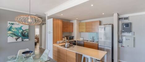 A modern kitchen with wooden cabinets, a stainless steel refrigerator, and a glass dining table with chairs.