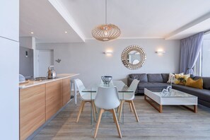 A modern living room with a glass coffee table, white chairs, a grey sofa, and a decorative mirror on the wall. - Horizon Bay 903 Fresh Beachfront Hideaway (Bloubergstrand)