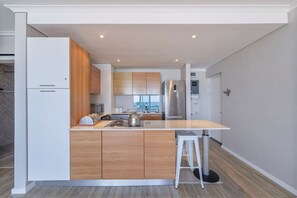 A modern kitchen with a central island, wooden cabinets, and stainless steel appliances. - Horizon Bay 903 Fresh Beachfront Hideaway (Bloubergstrand)