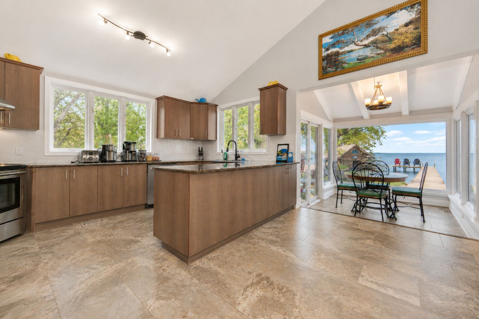A spacious kitchen with a large island, wooden cabinets, and a view of the sea through the glass door.