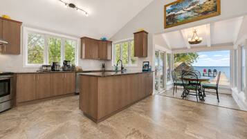 A spacious kitchen with a large island, wooden cabinets, and a view of the sea through the glass door.