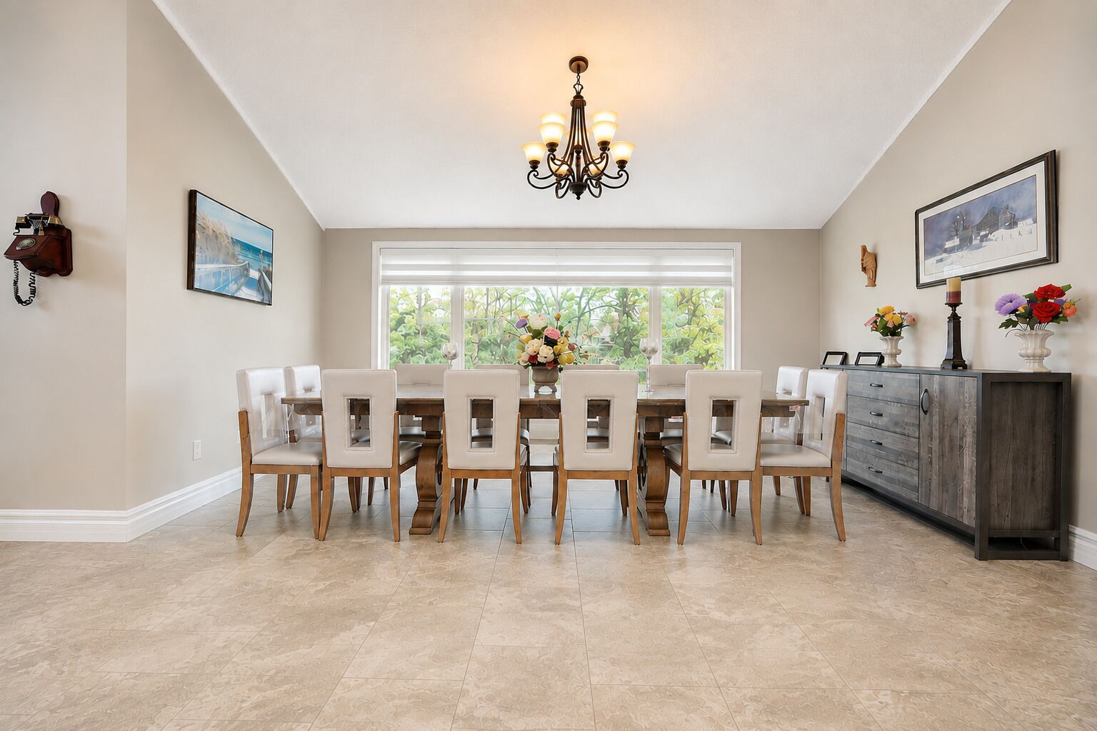 A dining area with a large table, chairs, a chandelier, and a window with blinds.