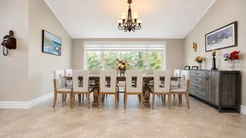 A dining area with a large table, chairs, a chandelier, and a window with blinds.