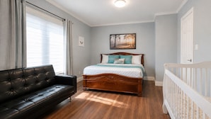 A bedroom with a bed, a black leather sofa, and a white crib. - Lakefront Lake Simcoe Retreat | Private Dock, Hot Tub & Sandy Shore (Georgina)