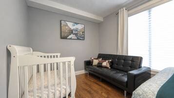 Une pièce avec un berceau blanc, un canapé en cuir noir et un tableau accroché au mur.