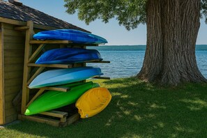 A wooden structure with kayaks stored under it, a tree, and a body of water in the background.