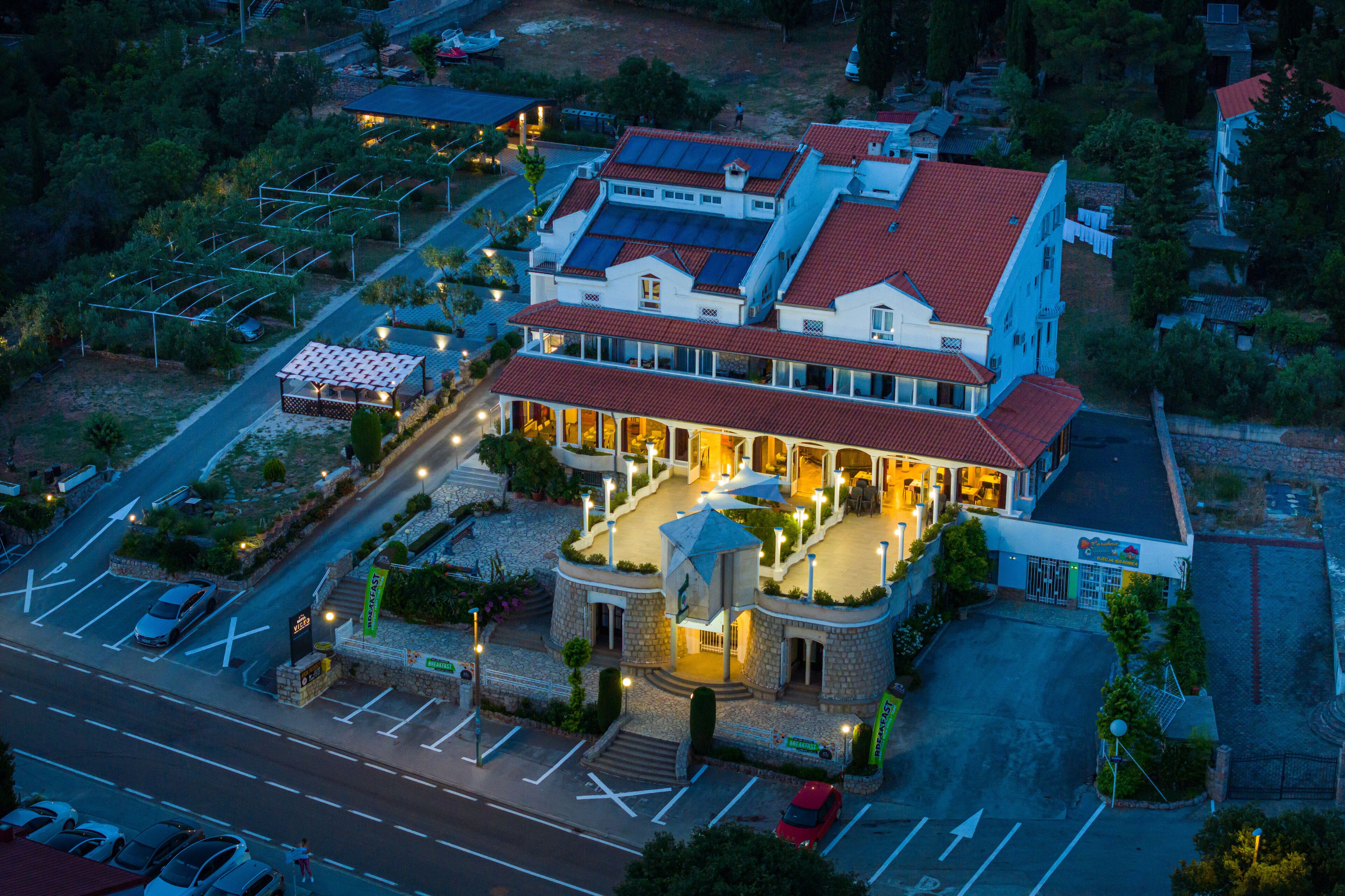 An aerial view of a hotel with a red-tiled roof, multiple stories, and a parking lot.