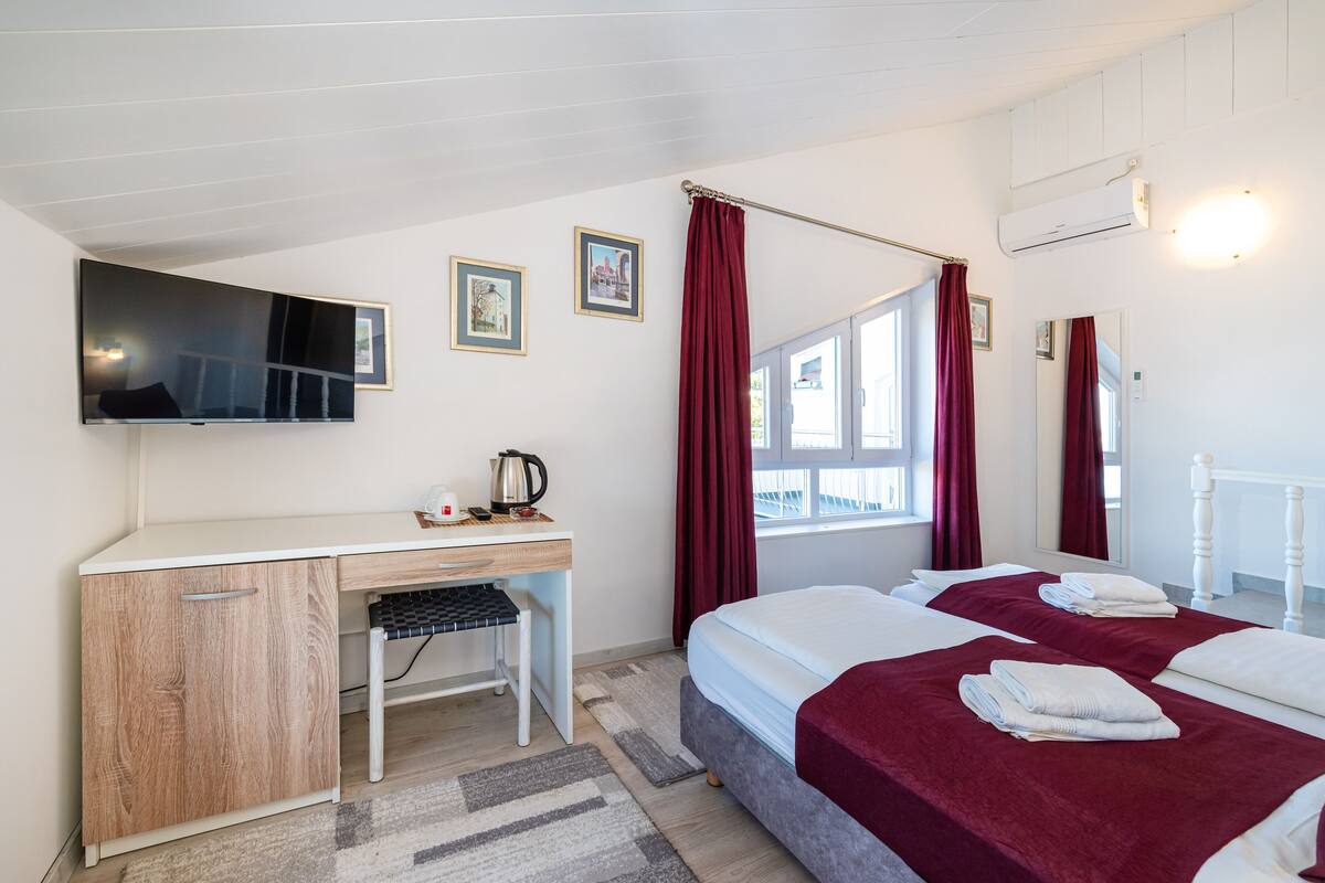 A hotel room with a desk, two beds, a TV, and a window with curtains.