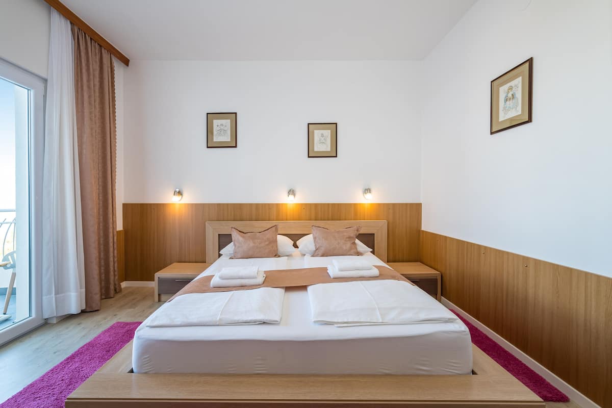 A neatly made double bed with white linens, two bedside tables with lamps, and a window with curtains.