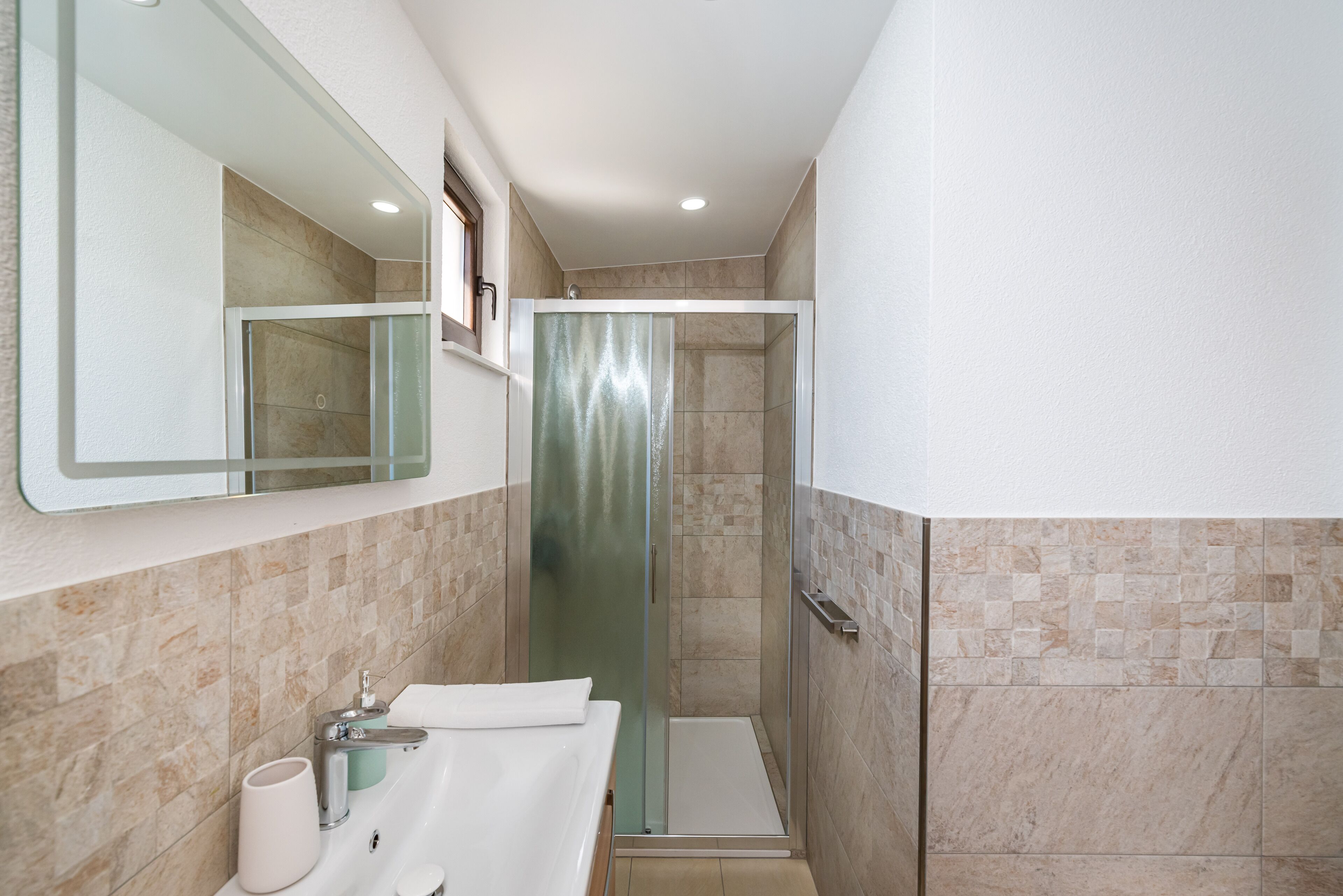 A bathroom with a glass shower enclosure, a double sink with a towel, and a mirror above the sink.