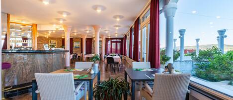Un hall d’hôtel avec un comptoir d’accueil en marbre, des chaises en osier blanc et des plantes en pot.