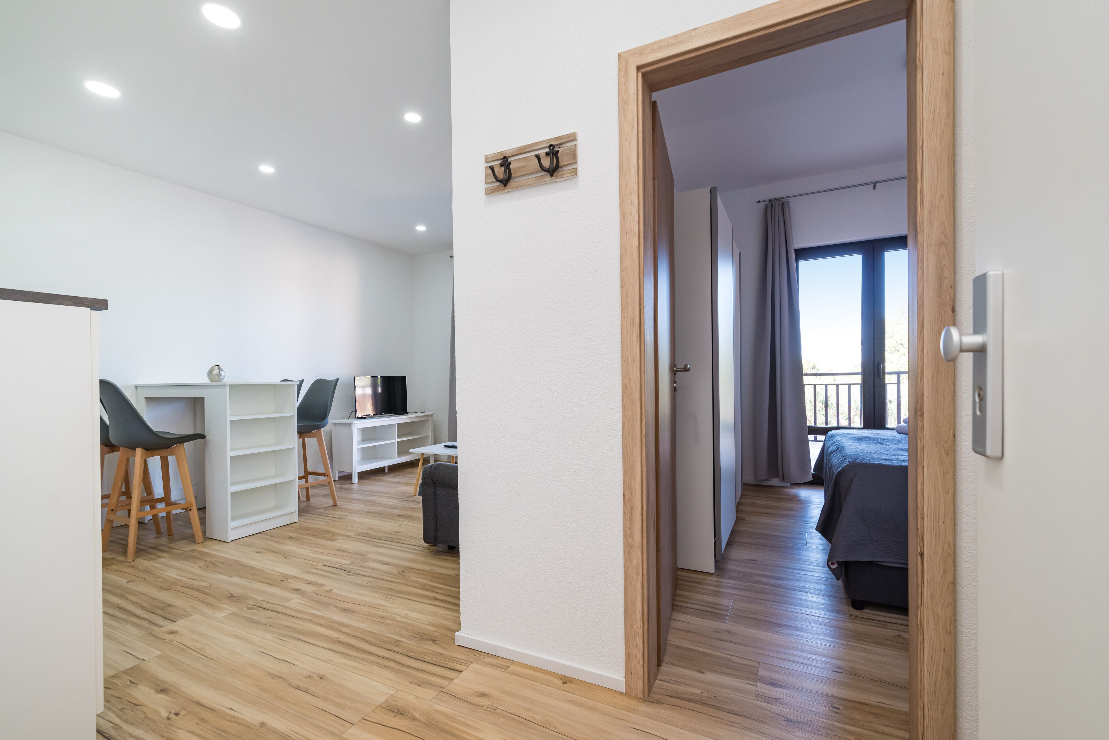 Una habitación moderna con suelo de madera, un escritorio con sillas, una cama y un balcón con cortinas.