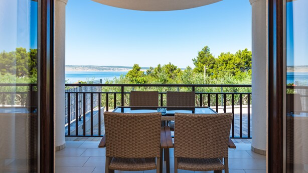 A balcony with a table and chairs, overlooking a scenic view of the sea and greenery. - Hotel Vicko (Starigrad)