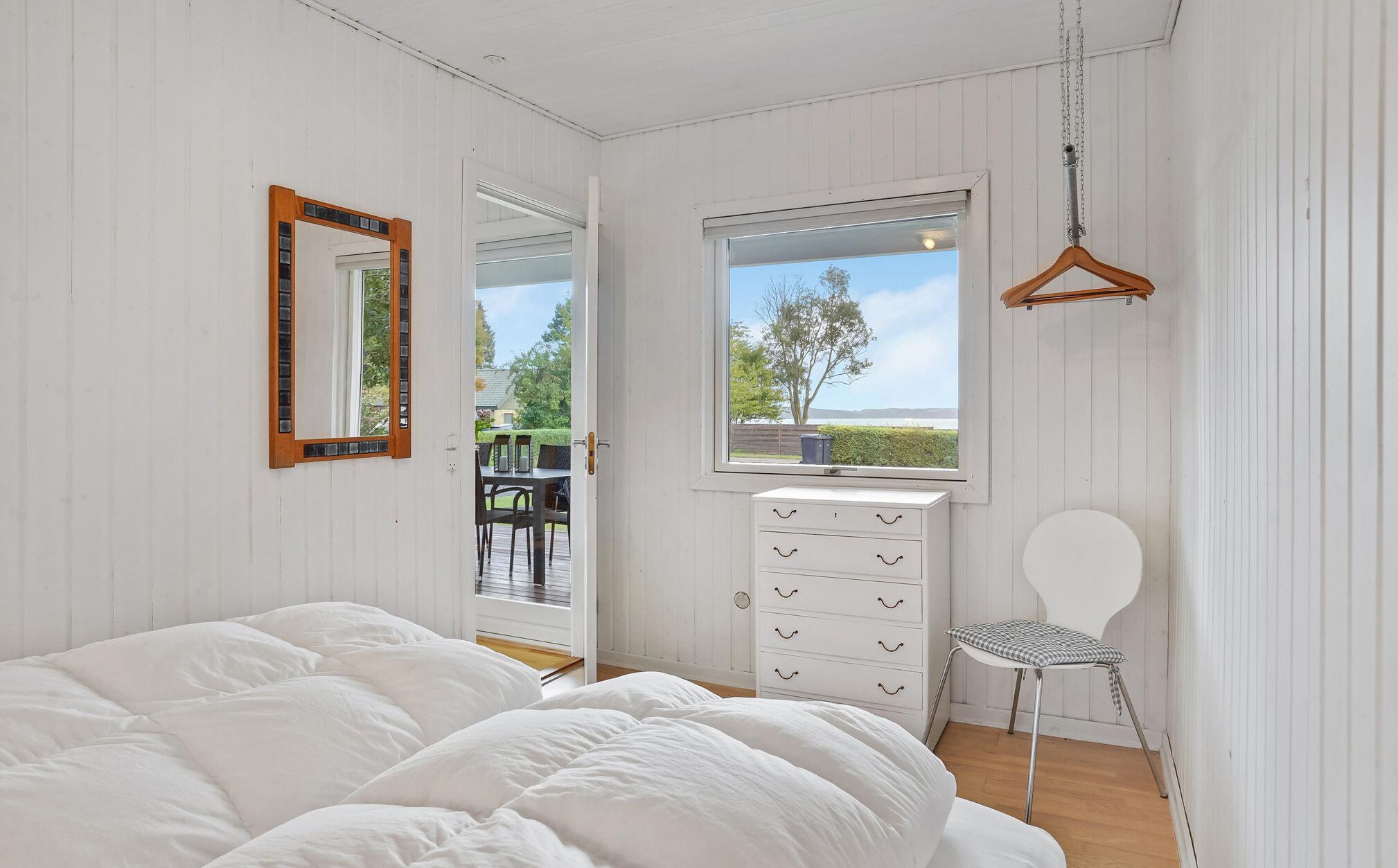 A bedroom with a bed, a dresser, a chair, a window with a view, and a hanging light.