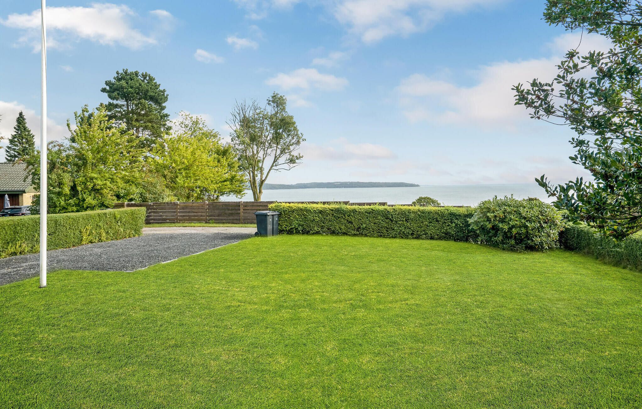 A well-maintained lawn with a flagpole, a wooden fence, and a view of the sea.