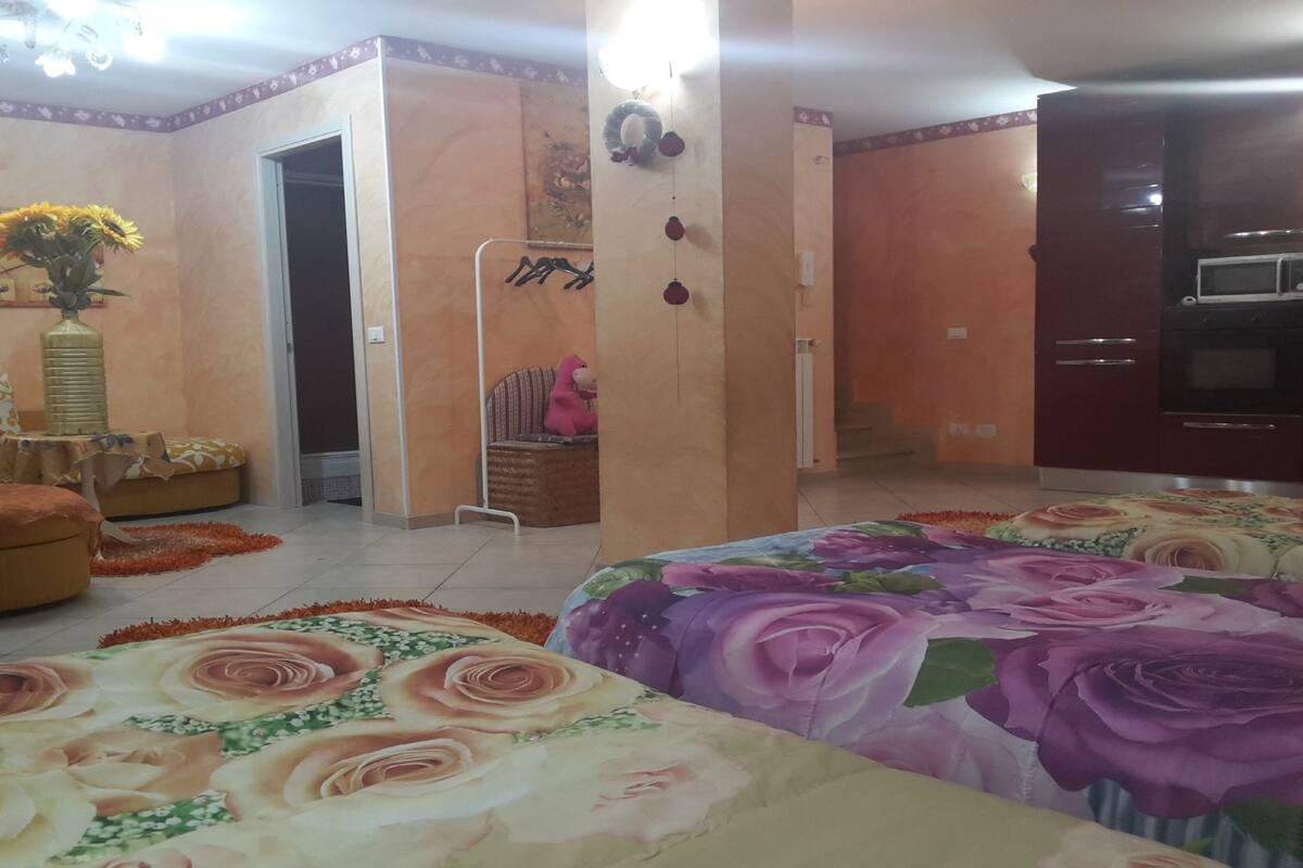 A bedroom with two beds, a sofa, a small table, and a chair. There is a doorway leading to another room.