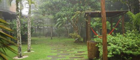 A garden pathway with stone tiles, surrounded by lush greenery and a wooden pergola structure.