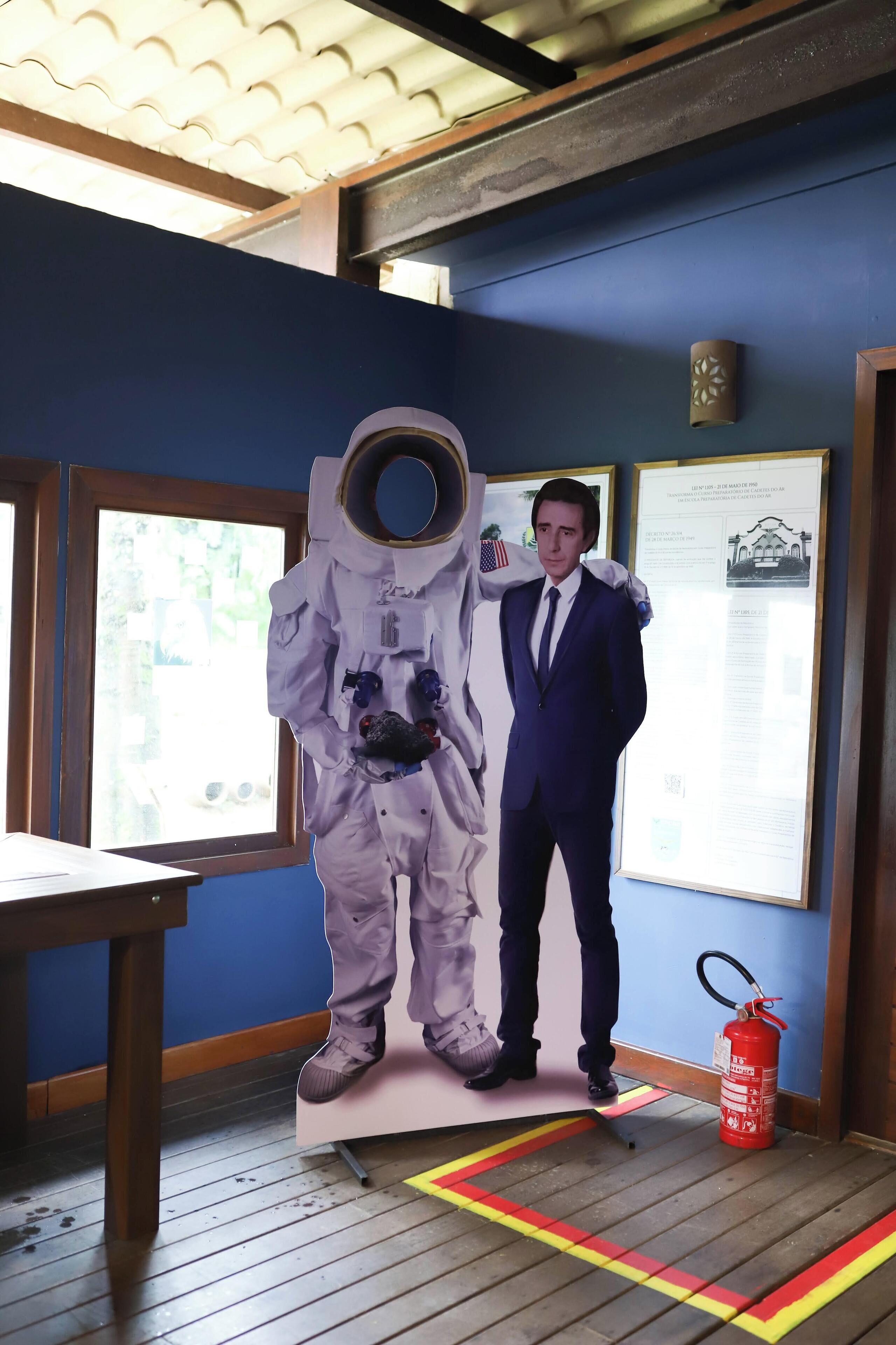 A room with a blue wall, a framed picture, a fire extinguisher, and a window.