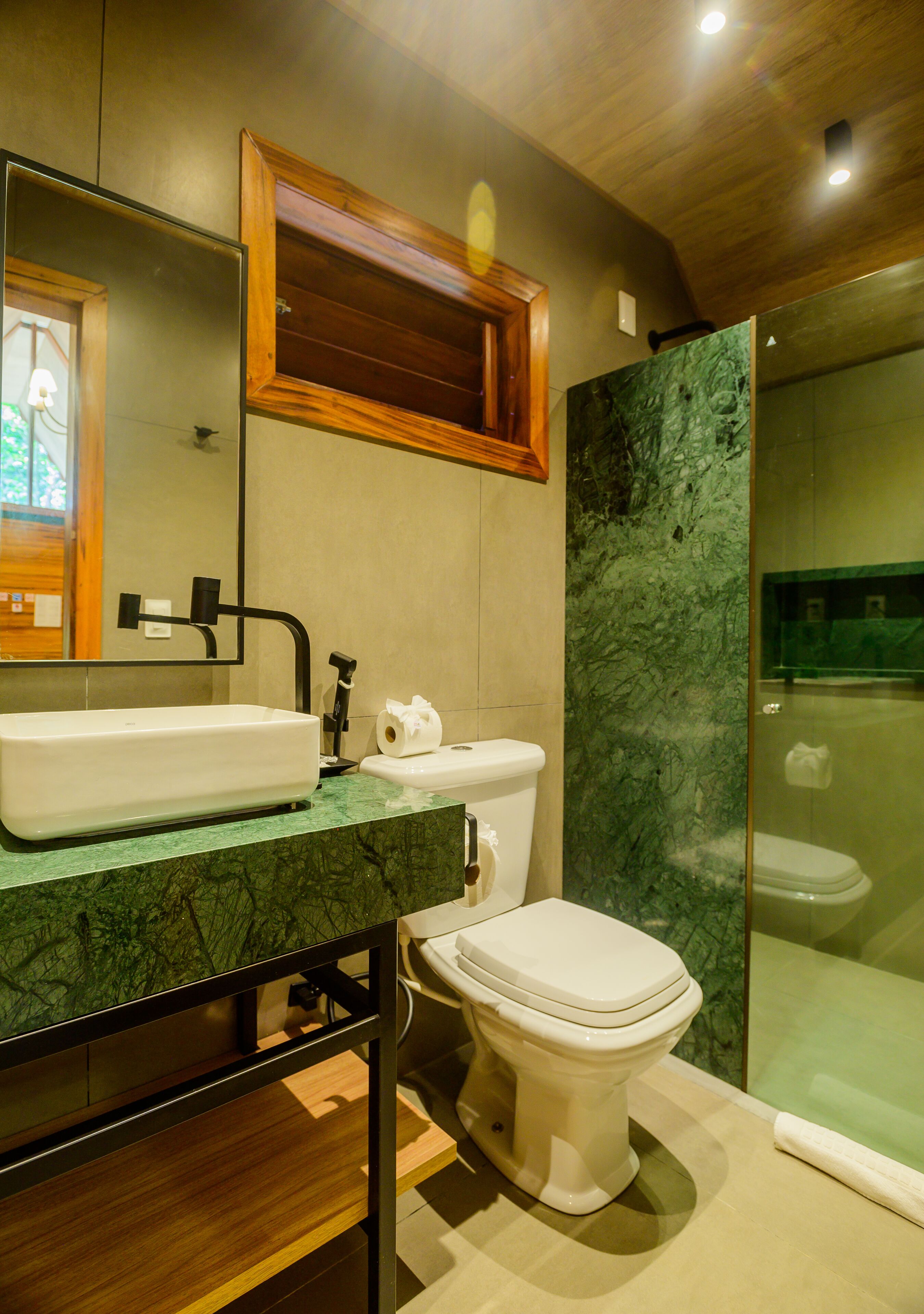 A modern bathroom with a marble sink, wooden vanity, a toilet, and a glass-enclosed shower.