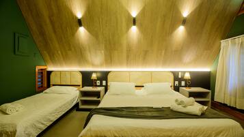 Habitación de hotel con dos camas individuales, una cama más grande, techo de madera, lámparas fijadas a la pared y una mesita de noche con lámpara.
