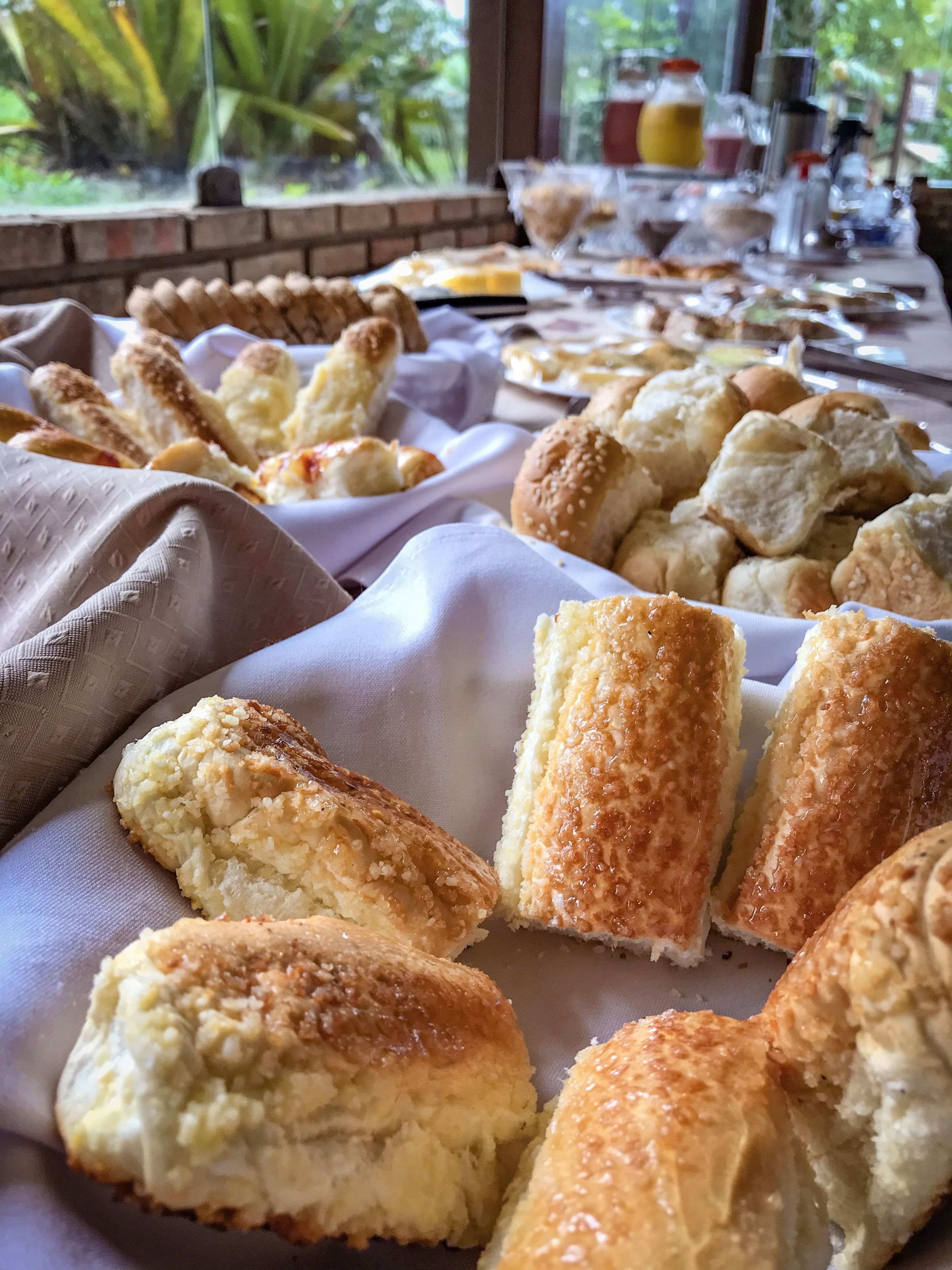 A table with various baked goods, including bread rolls and pastries, in a room with a view of greenery outside.