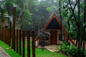 A small, triangular-roofed cabin surrounded by lush greenery and a wooden fence.