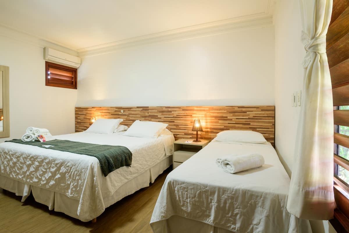 A hotel room with two beds, a wooden headboard, a mirror, and a window with blinds.