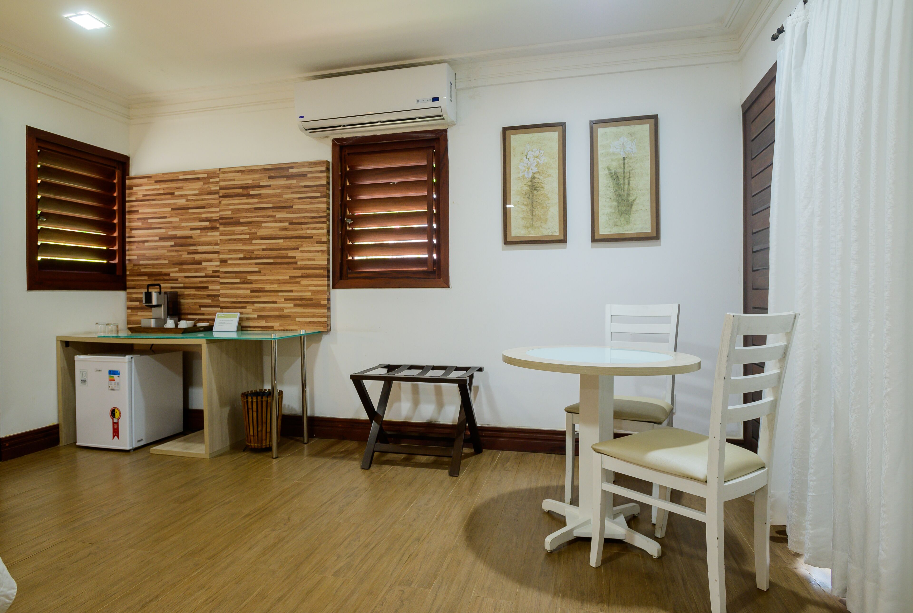 A compact room with a kitchenette, a dining table with a chair, and two framed pictures on the wall.