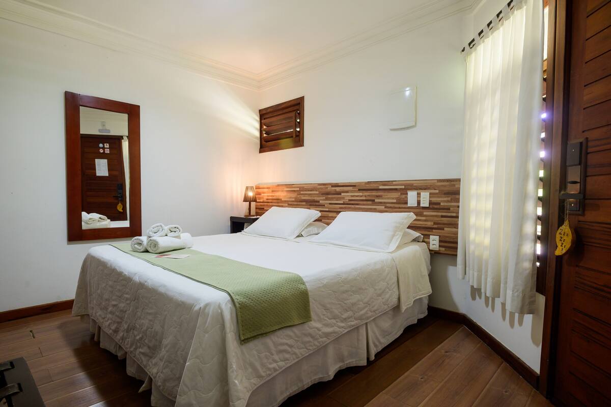 A neatly made bed with a green blanket, a wooden headboard, a nightstand, and a mirror on the wall.