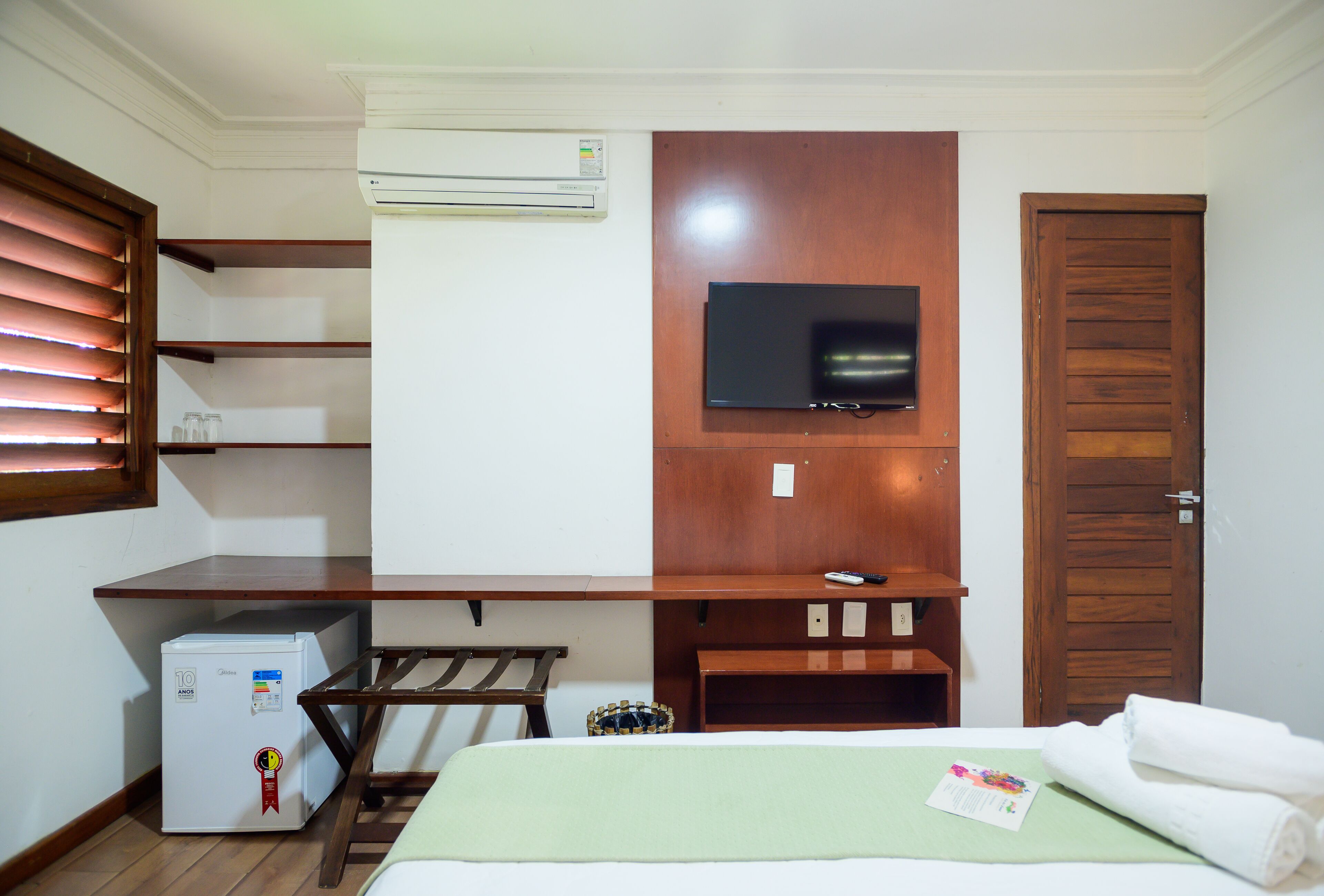 Una habitación de hotel con una cama, un escritorio, un televisor, aire acondicionado y un armario de madera.