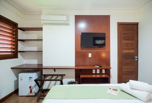 A hotel room with a bed, a desk, a television, an air conditioner, and a wooden wardrobe.
