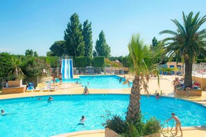 Una amplia piscina al aire libre con varias pistas de natación, rodeada de palmeras y sillas de descanso.