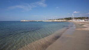 A beach with clear water, a rocky outcrop, and sailboats. - Beautiful T2 apartment in residence standing with pool facing the sea (Six-Fours-les-Plages)