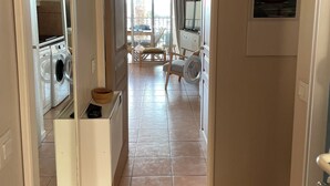 A hallway leading to a living area with a view of the outside, a washing machine, and a dining area with chairs and a table. - Beautiful T2 apartment in residence standing with pool facing the sea (Six-Fours-les-Plages)