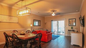 Un coin repas avec une table et des chaises en bois, un canapé rouge et un ventilateur de plafond.