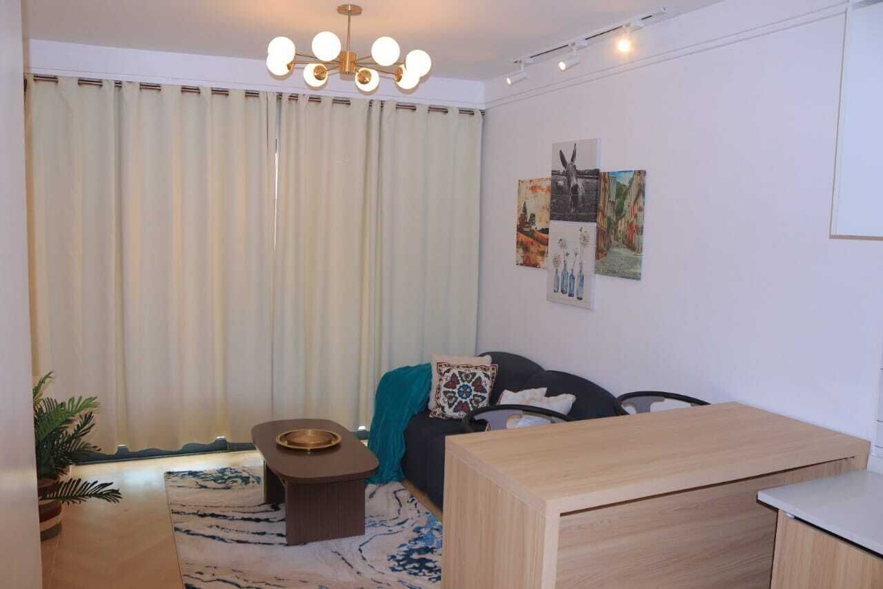 A modern living room with a wooden coffee table, a black sofa with patterned cushions, a teal throw blanket, and a wall-mounted artwork.