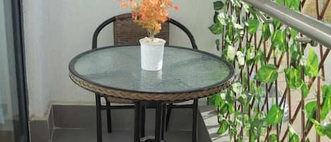 A balcony with a round table and two wicker chairs, a potted plant, and a metal railing.